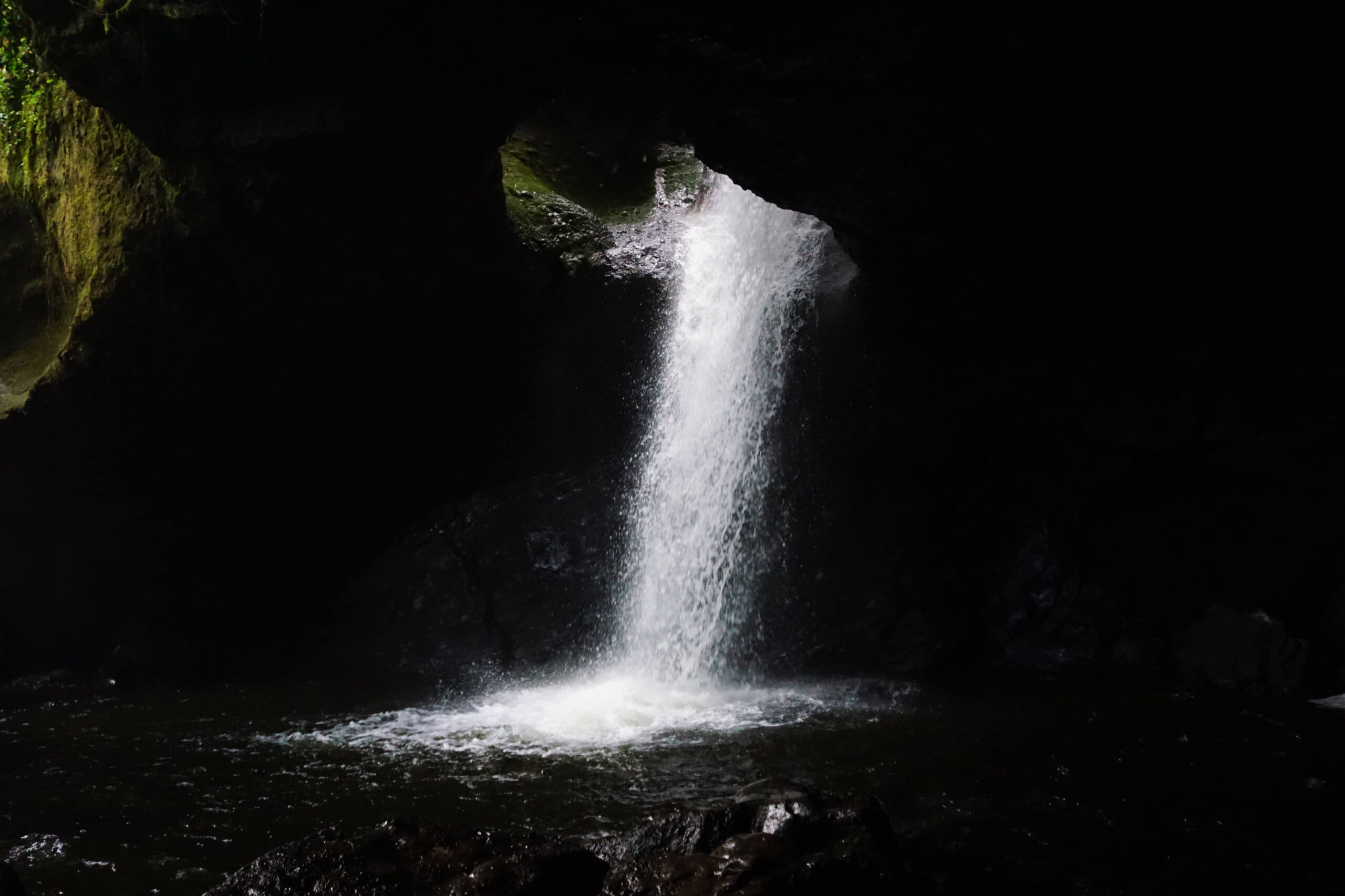 Cueva Del Esplendor, a waterfall flowing through the roof of a dark cave into the pool below.